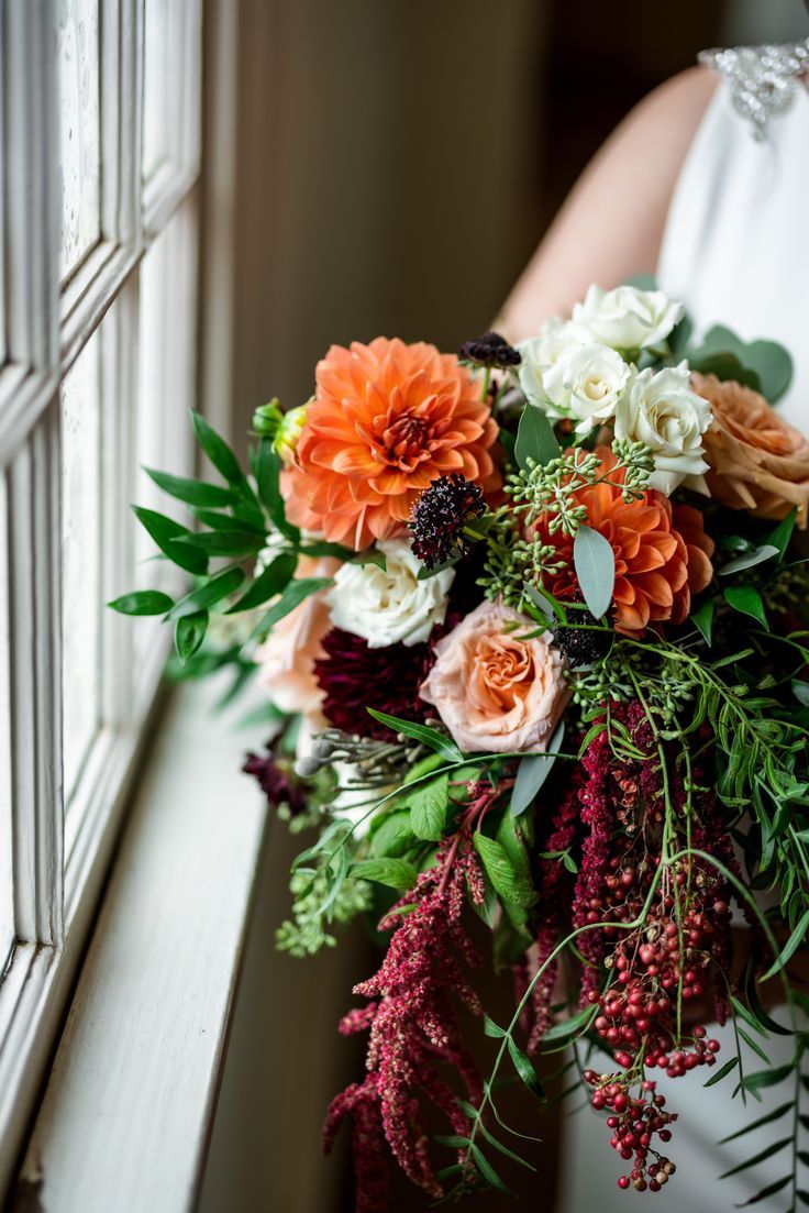 a bride holding a bouquet of flowers in her hand near a window sill with greenery