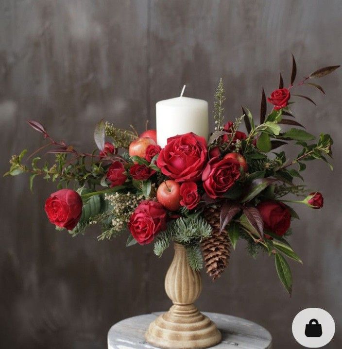 a vase with roses and greenery on a table next to a white candle holder