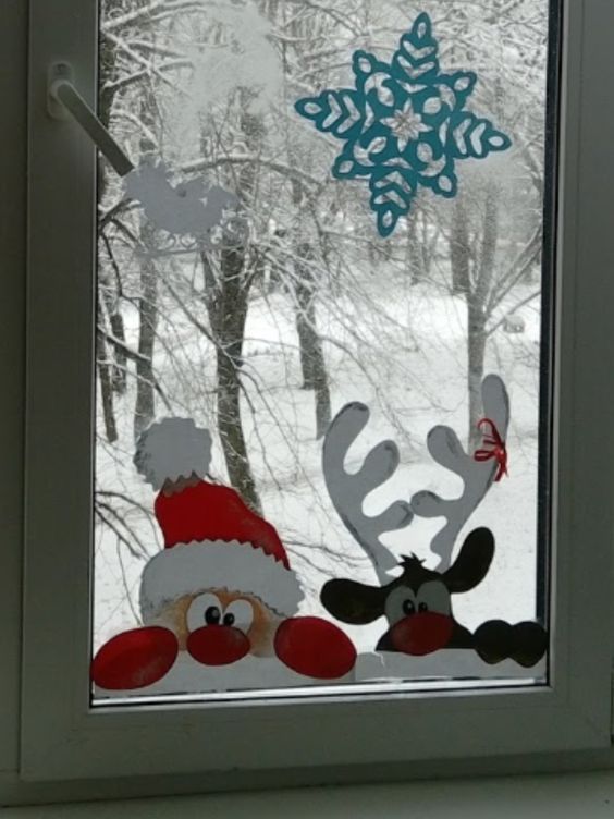 a window with reindeers and snowflakes on it in front of a snowy forest