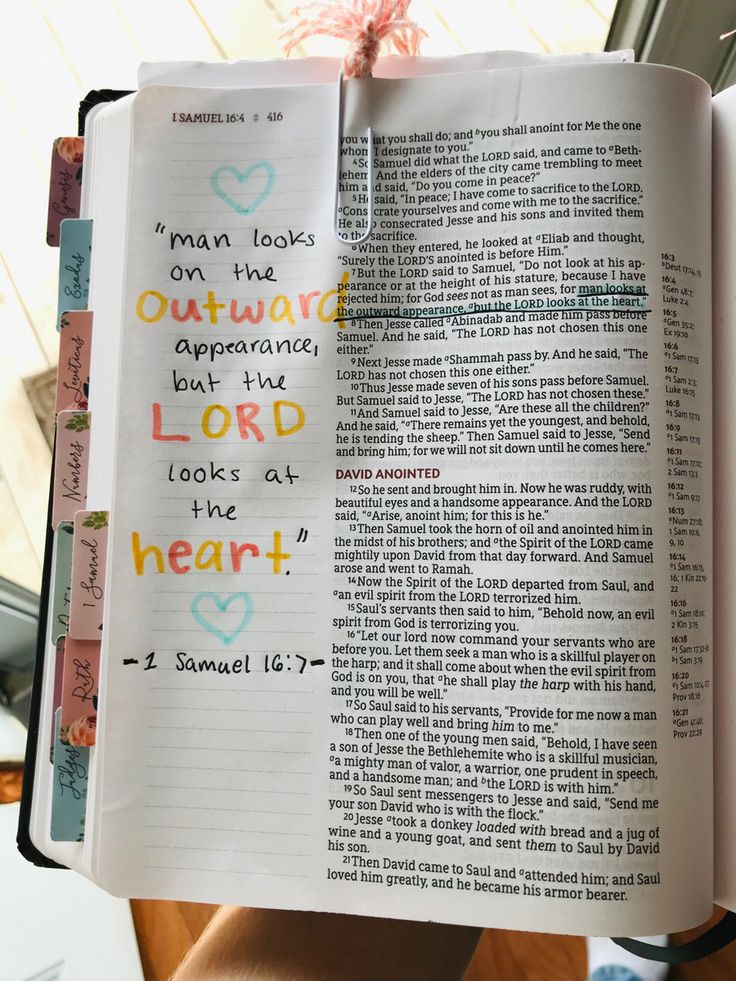 an open bible with handwritten words on the pages and a pink ribbon tied to it