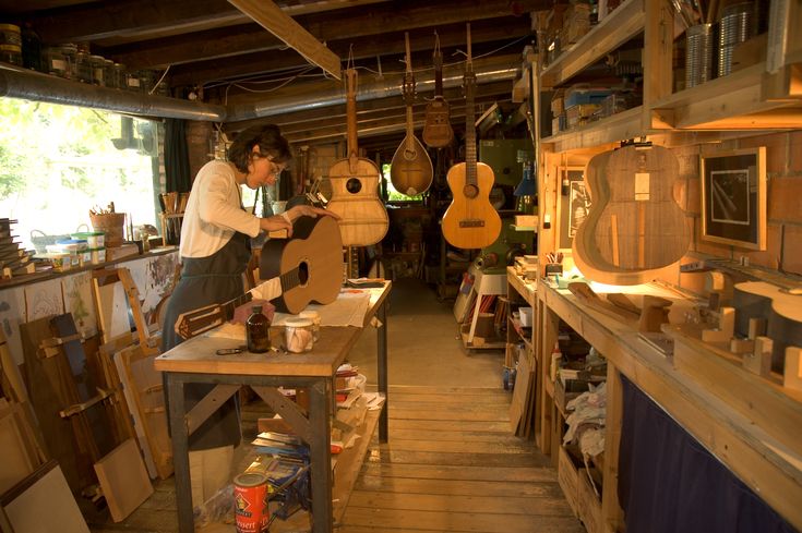 a woman is working in an art studio with guitars hanging from the ceiling and shelves