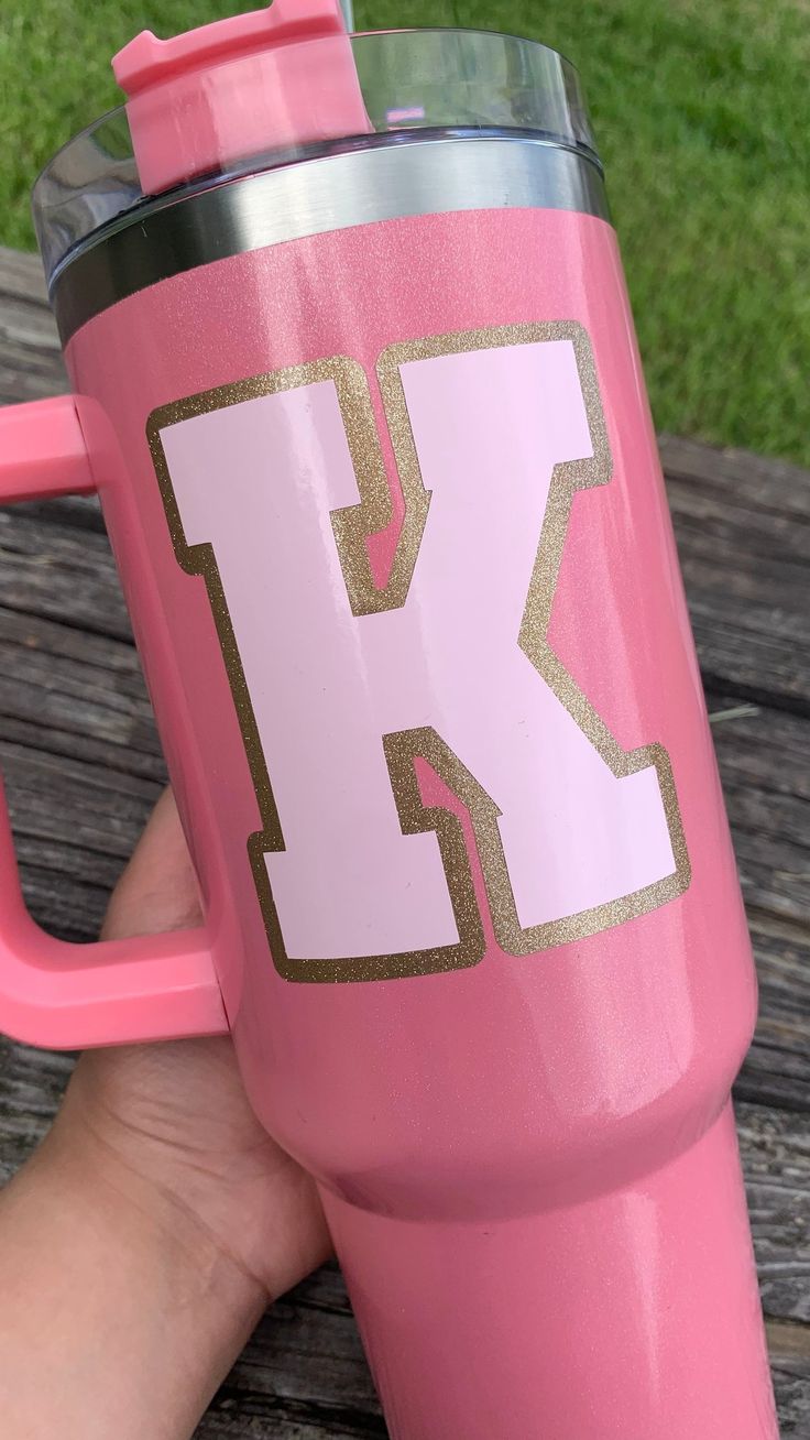 a person holding a pink and gold colored cup with the letter k on it's side