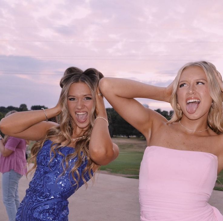 two beautiful women standing next to each other in front of a pink and blue sky