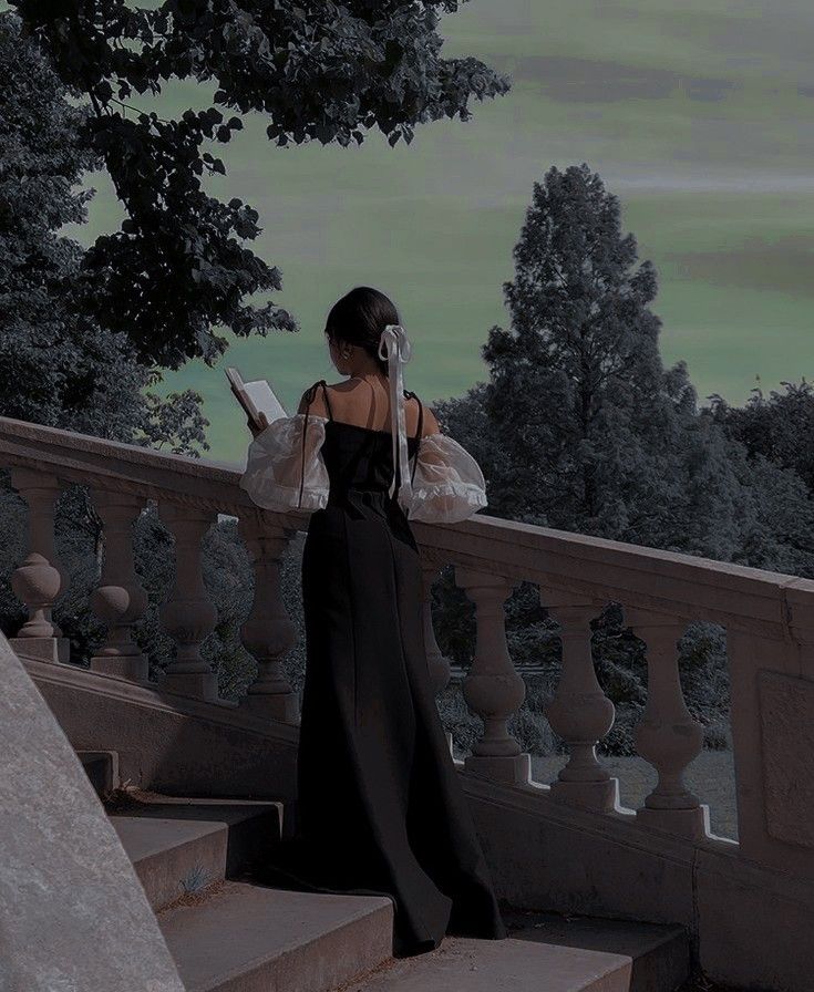 a woman is standing on some stairs and looking at her cell phone while wearing a long black dress