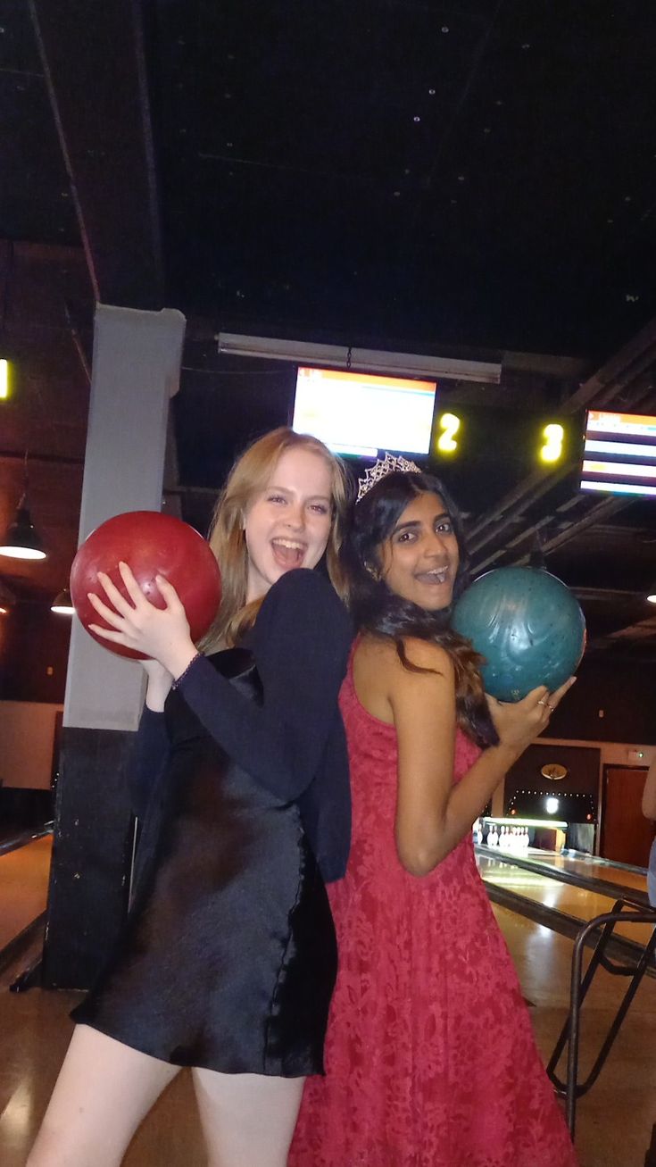 two women in dresses holding bowling balls and posing for the camera with their arms around each other