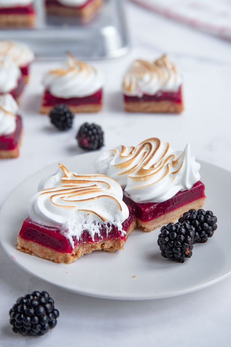 some desserts are sitting on a white plate with blackberries and raspberries