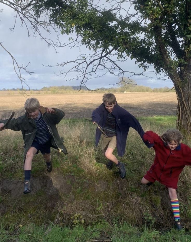 three children are playing in the mud near a tree and some grass with one child on it's back