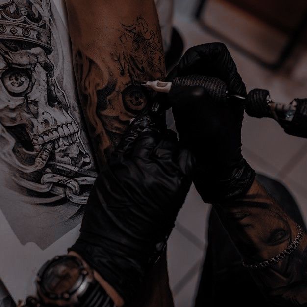 a man with tattoos on his arm getting inked by another person in black gloves