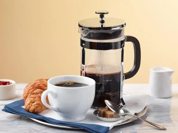 a cup of coffee and some croissants sitting on a table next to a french press