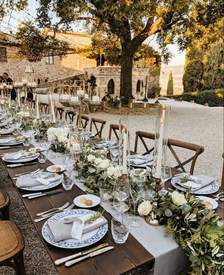 a long table set with place settings and flowers on it for an outdoor dinner party