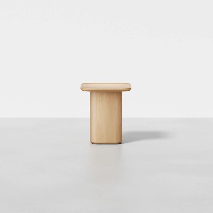 a small wooden stool sitting on top of a white floor next to a gray wall