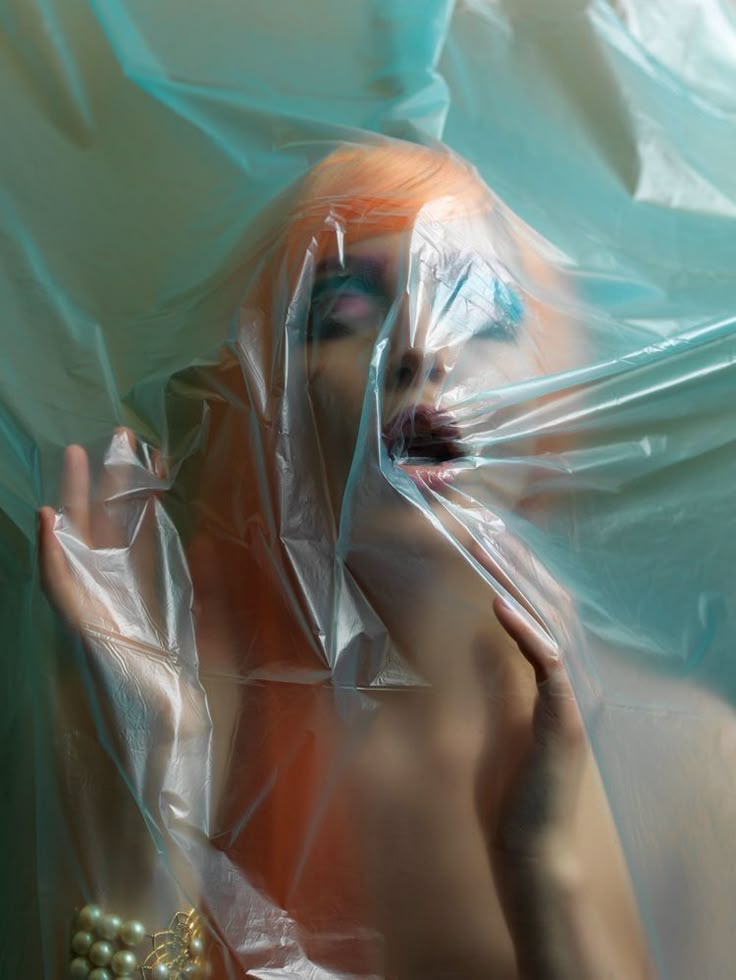 a woman with orange hair is wrapped in plastic and holding her hand up to her face