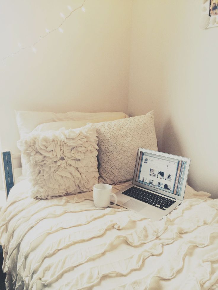 a laptop computer sitting on top of a bed next to pillows and a cup with coffee