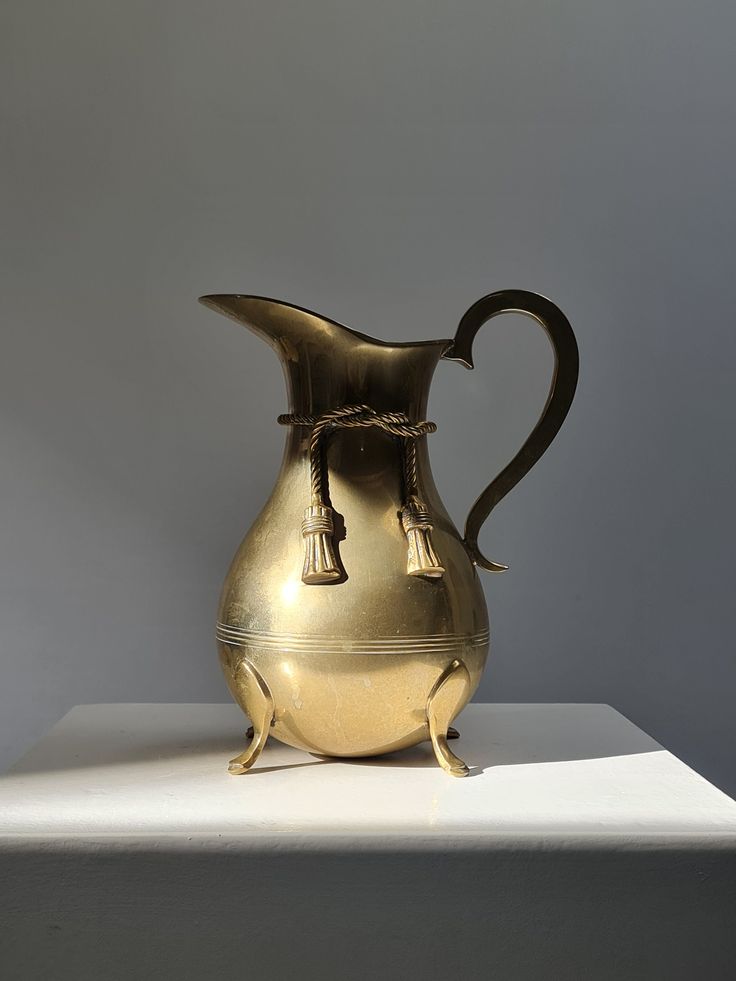 a gold colored pitcher sitting on top of a white counter next to a gray wall