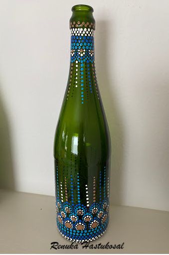 a green bottle with designs on it sitting on a table next to a white wall