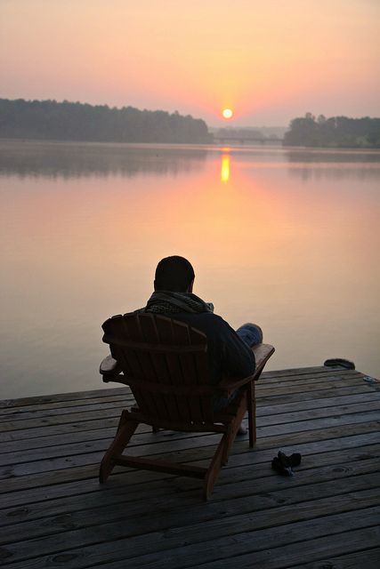 a person sitting in a chair on a dock with the sun setting over water behind them