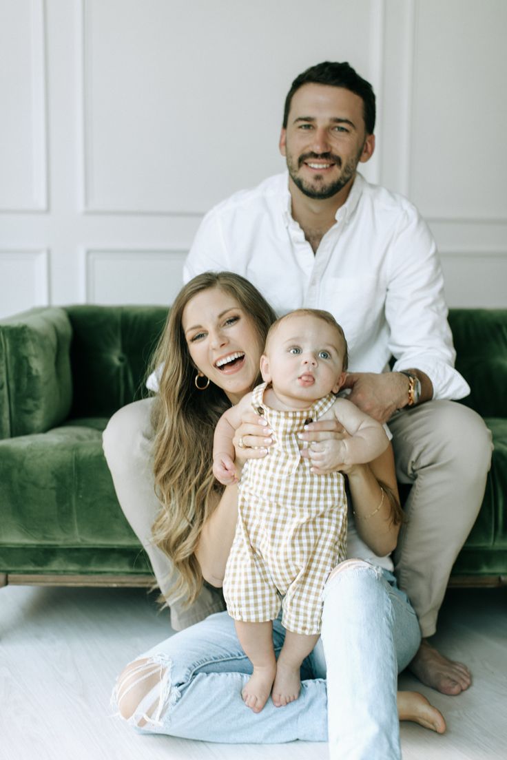 a man and woman sitting on a couch with a baby in their lap smiling at the camera