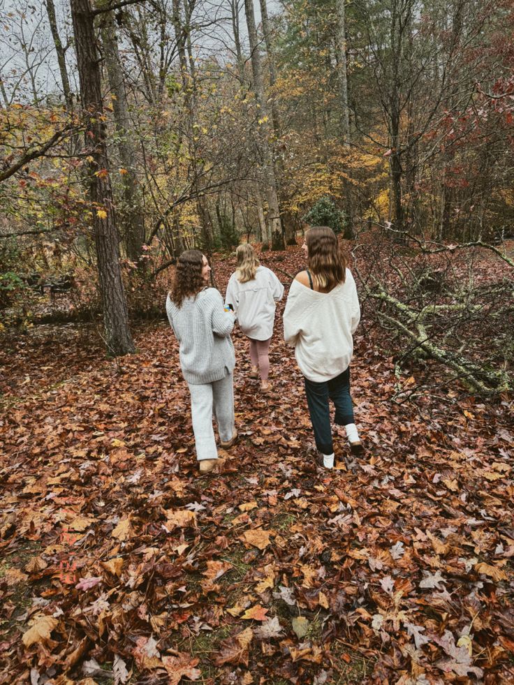 three girls walking through leaves in the woods