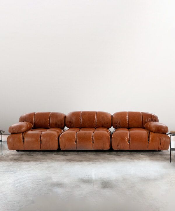 a brown leather couch sitting on top of a white floor next to a table with two end tables