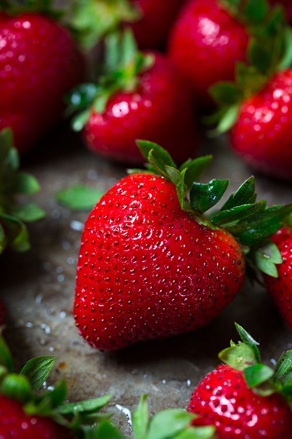 a group of strawberries sitting on top of a table next to each other with green leaves