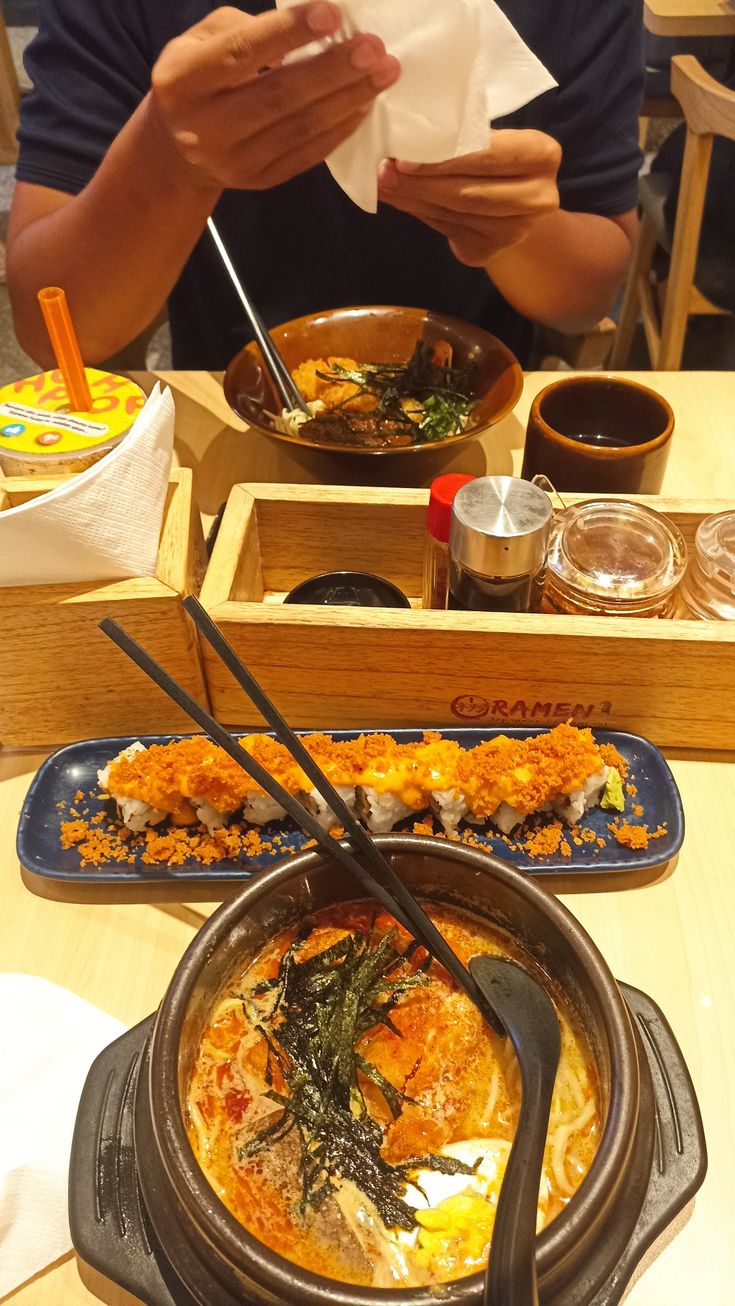 a person sitting at a table with bowls of food and chopsticks in front of them