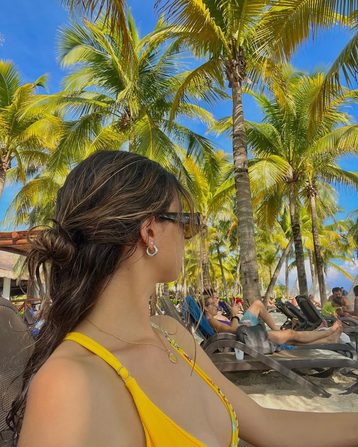 a woman in a yellow top is on the beach with palm trees and lounge chairs