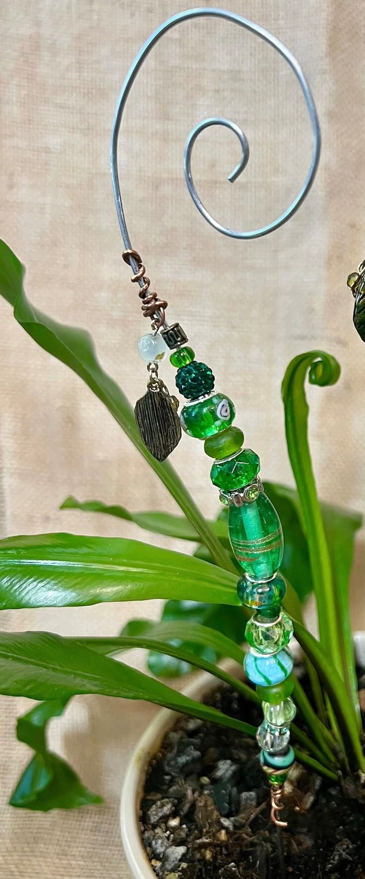 a green glass beaded necklace hanging from a wire on top of a potted plant