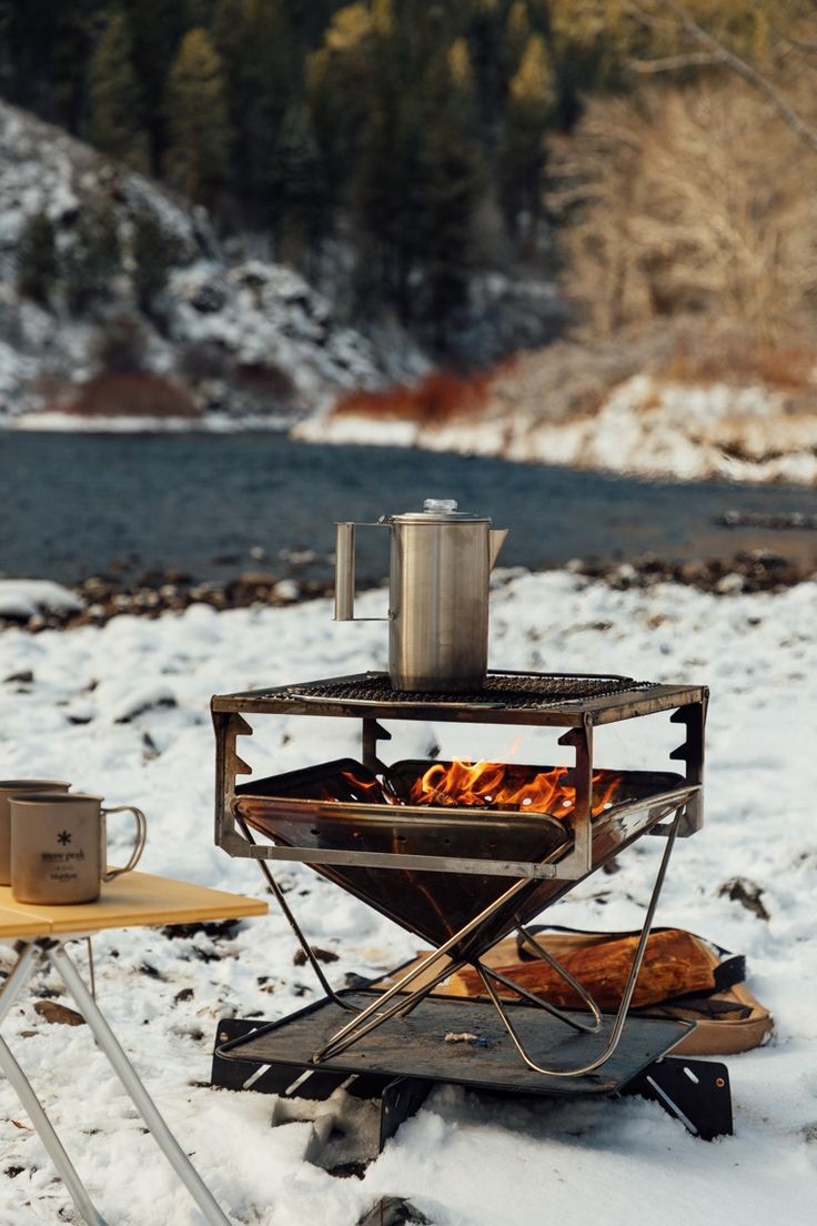 an open fire pit sitting on top of snow covered ground next to a table and chairs