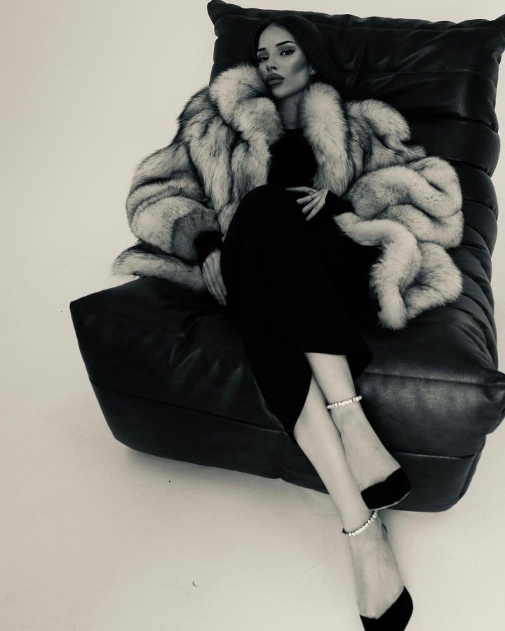 a woman sitting on top of a black couch next to a large fur coat over her head