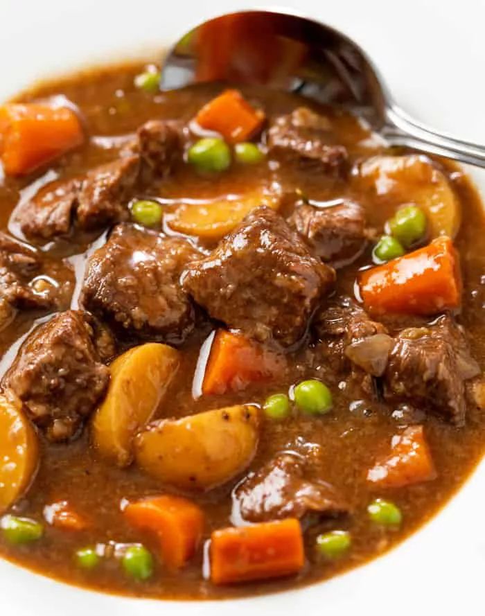 a bowl of beef stew with carrots, potatoes and peas