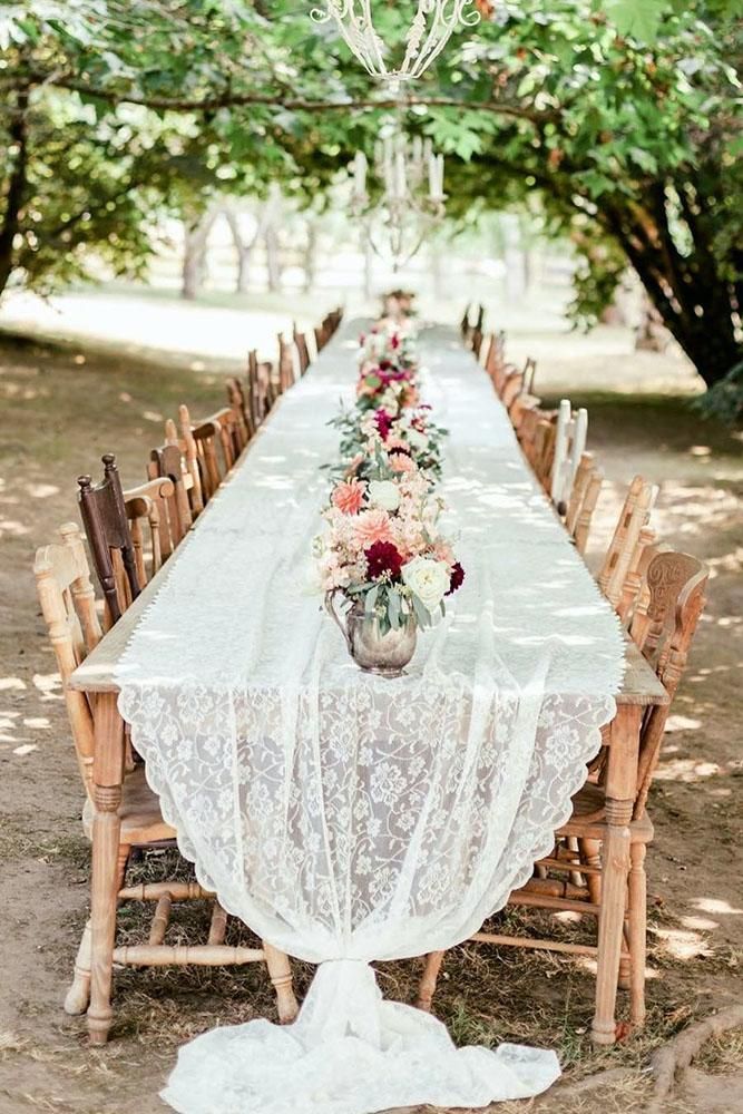 a long table is set with flowers and lace on it for an outdoor wedding reception