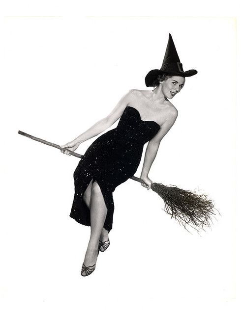 a black and white photo of a woman dressed as a witch flying through the air