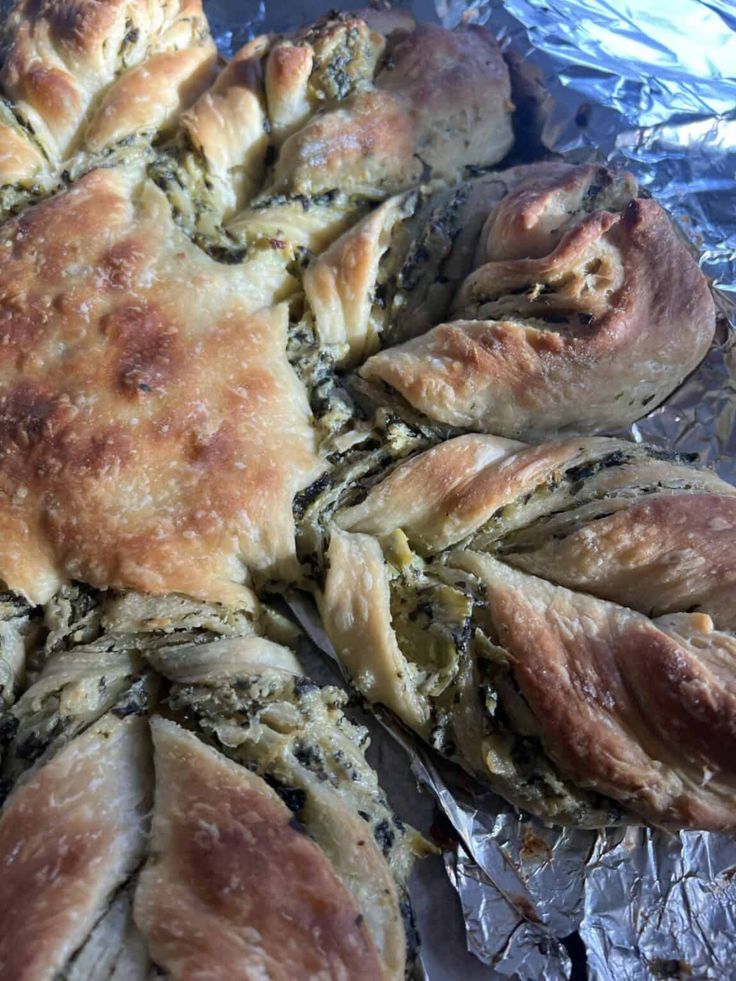 baked bread with spinach and cheese on aluminum foil lined up in the shape of flowers