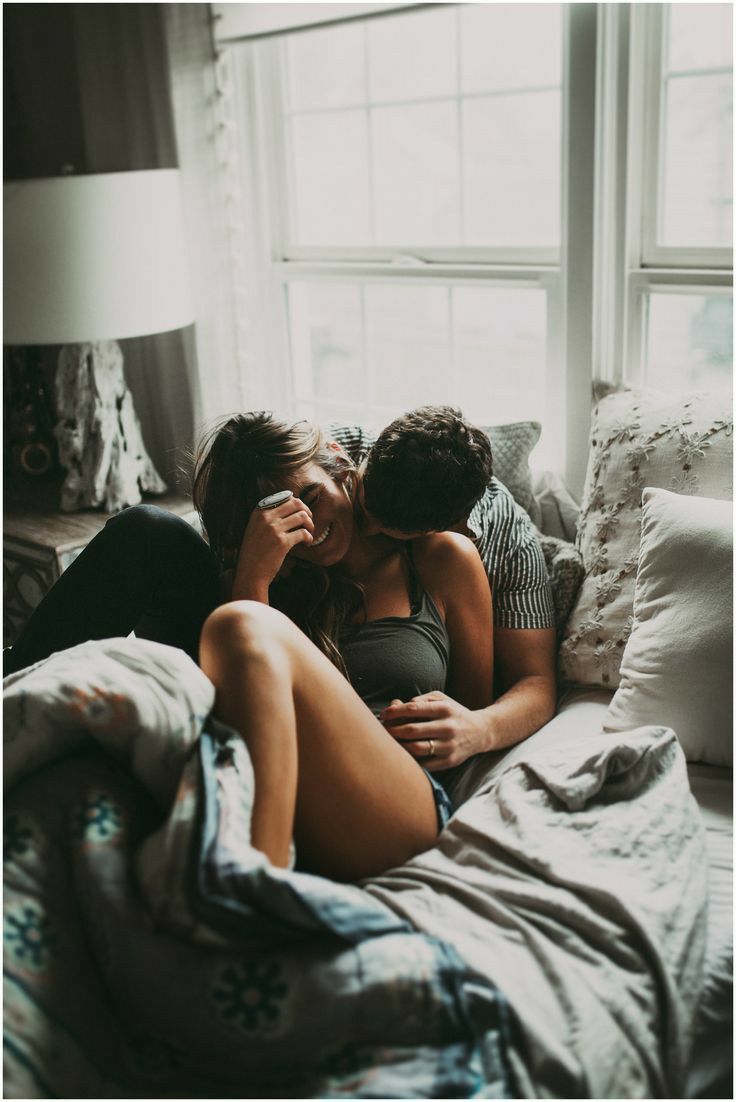 two people laying on a bed kissing each other in front of a window with the sun shining through