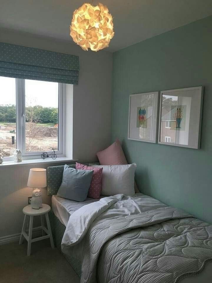 a bed sitting under a window next to a lamp and a table with a light on it