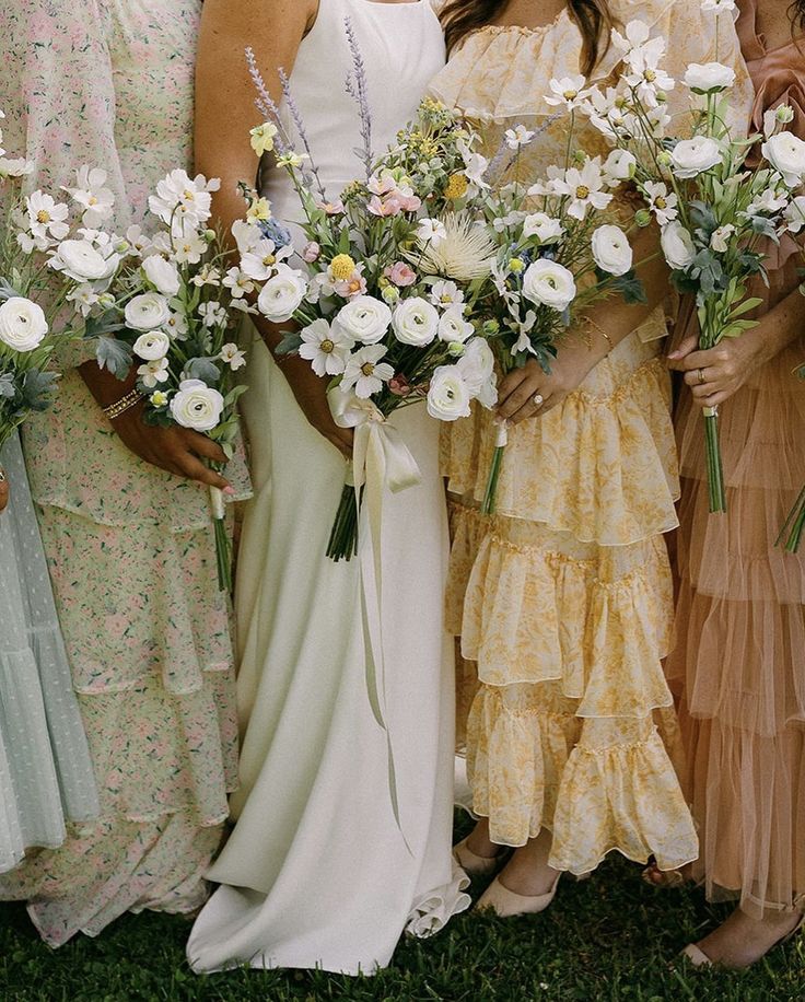 a group of women standing next to each other in dresses holding bouquets of flowers