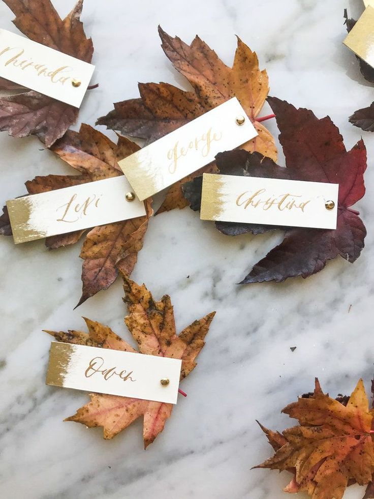 autumn leaves with name tags on them laying on a marble countertop in the fall