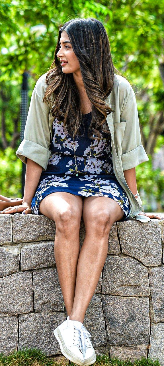 a woman sitting on top of a stone wall with her legs crossed and looking off to the side