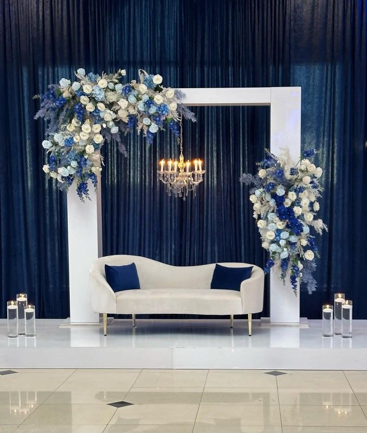 a white couch sitting under a chandelier in front of a blue and white curtain