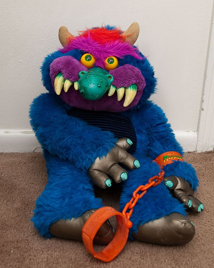 a blue and purple monster stuffed animal sitting on the ground next to a orange leash