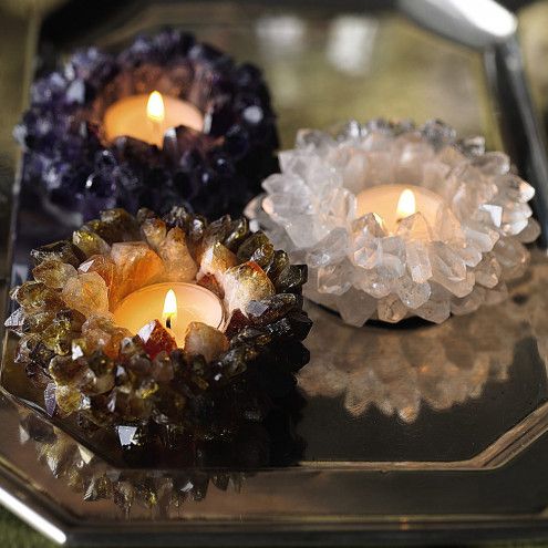 three candles sitting on top of a metal tray with crystal pieces around it and one candle lit in the middle