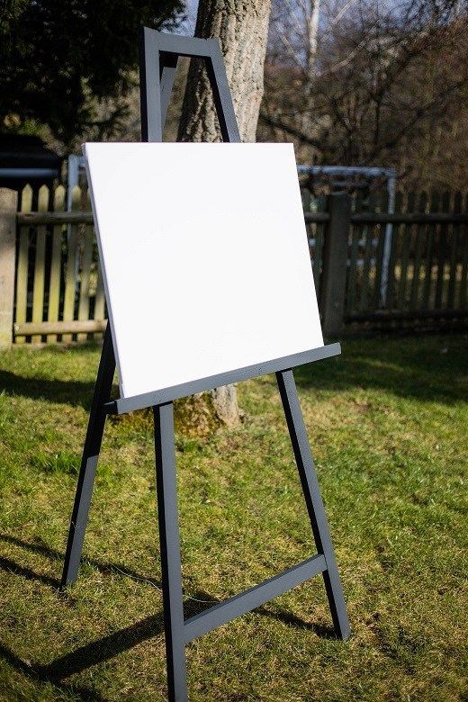 an easel stands in the grass next to a tree and fence, with a white board on it