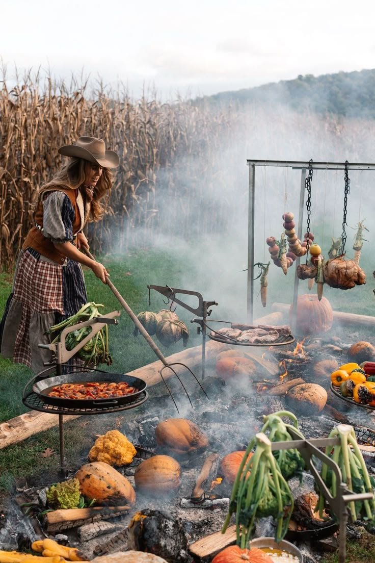 a woman grilling vegetables and corn on the cob in front of an open fire