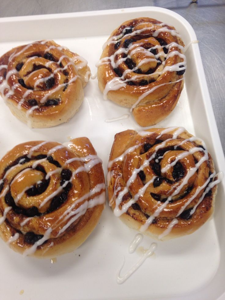 four cinnamon rolls sitting on top of a white tray with icing drizzled around them