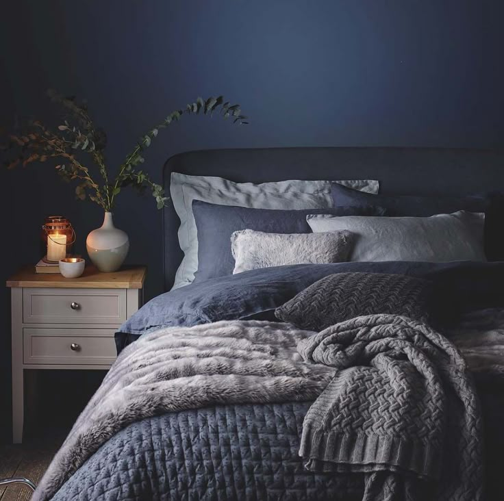 a bedroom with dark blue walls and grey bedding, white nightstands and plants