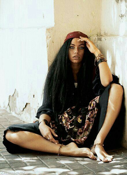 a woman sitting on the ground with her hands to her head and wearing a bandana