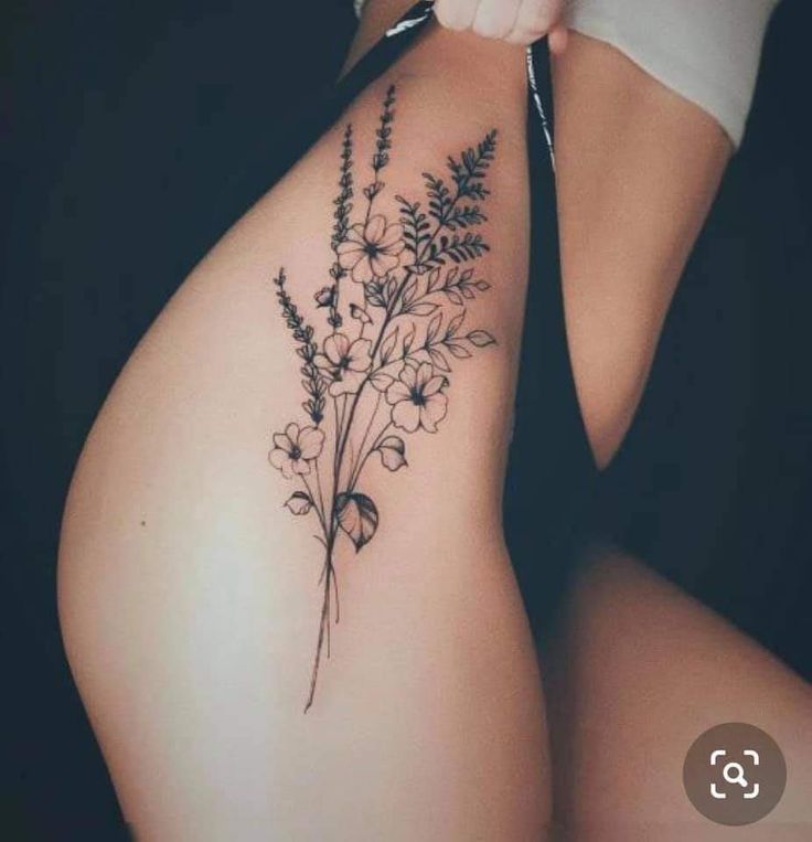 a woman's thigh with flowers and leaves tattoo on her side ribcage