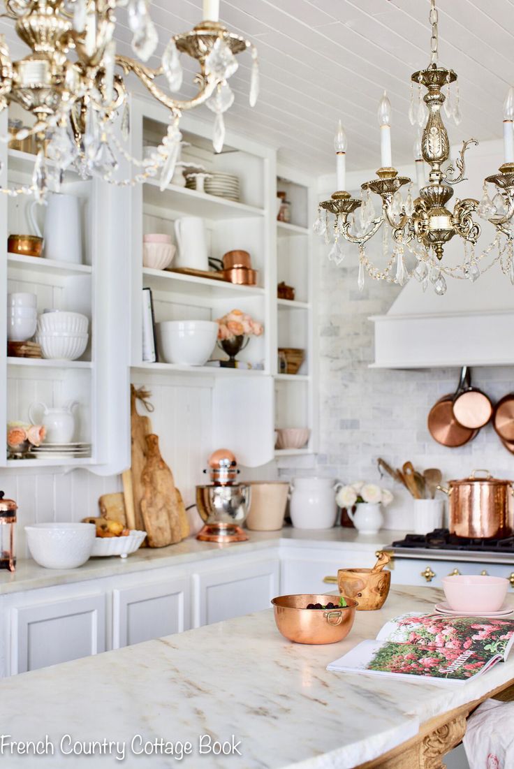 a kitchen filled with lots of white counter tops and gold chandelier hanging from the ceiling