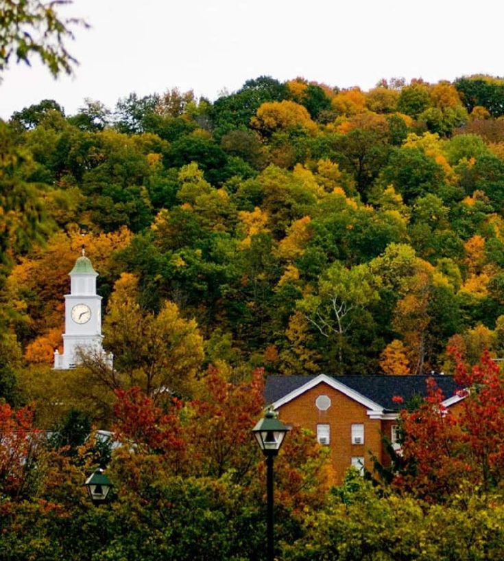 a clock tower on top of a building in front of trees with fall foliage around it