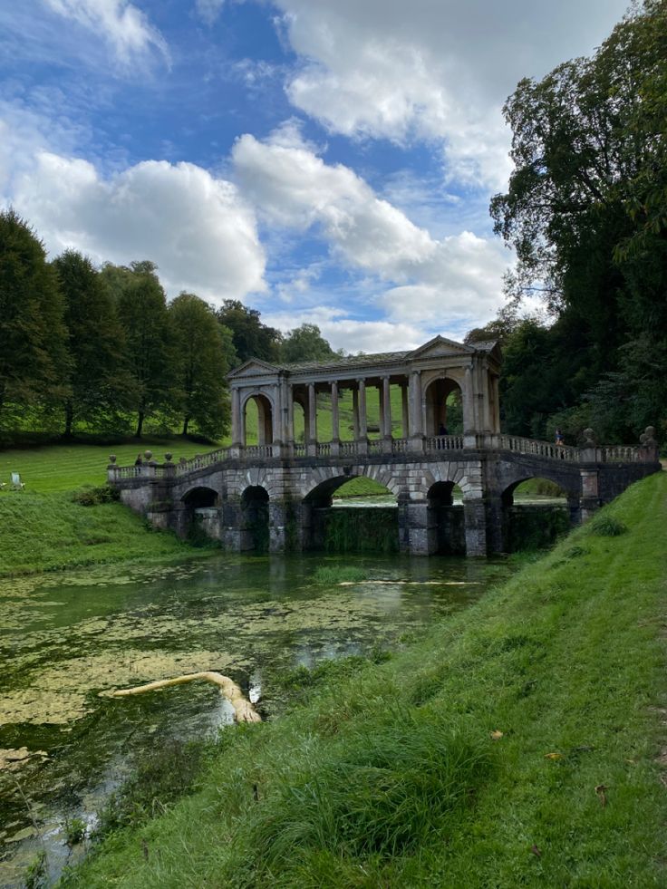 a bridge over a body of water in the middle of a lush green park with lots of trees